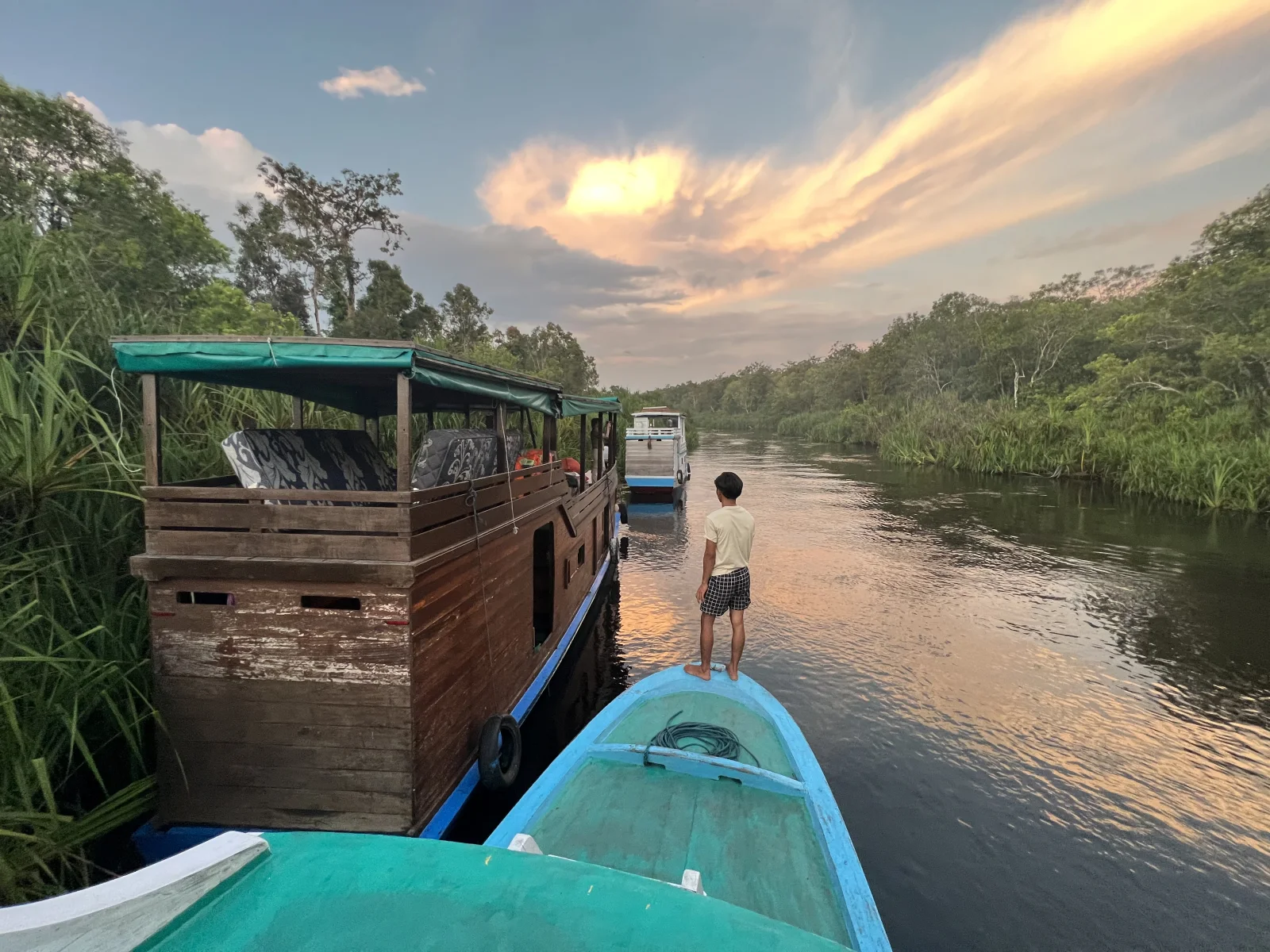 Una embarcación turística de madera navega por el río Sekonyer al atardecer.