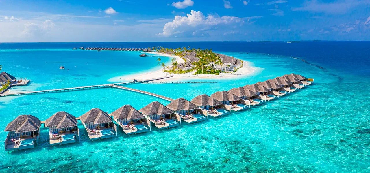 Una isla de Maldivas aparece rodeada de agua turquesa y villas sobre el mar.